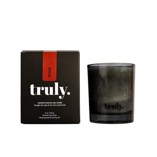 Black candle with 'truly' branding next to its packaging on a white background