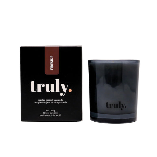 Black candle with 'truly' branding next to its packaging on a white background